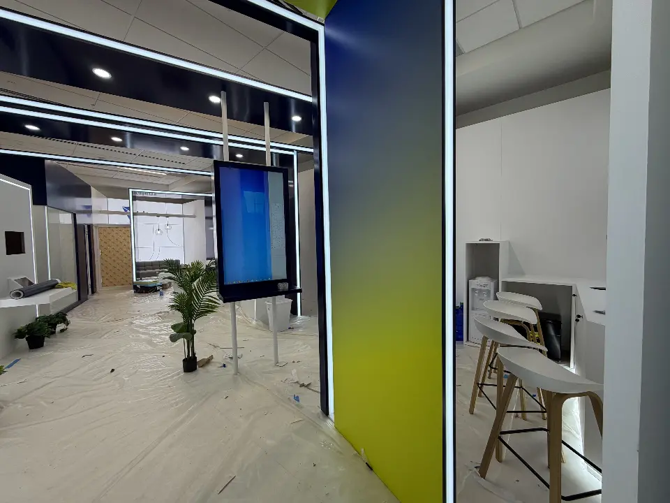 Gradient portal column beside a pole-mounted display screen and white bar stools at a counter