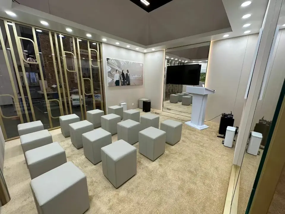 Enclosed presentation room with rows of grey cube seats, a white lectern and a screen