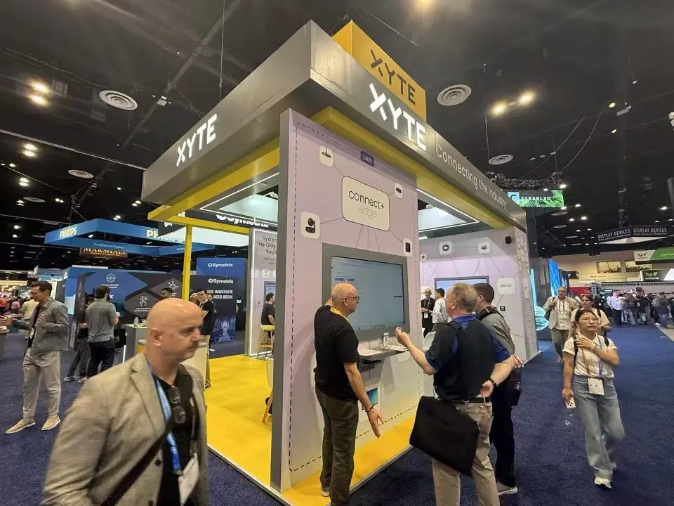 XYTE booth with yellow header, light grey walls and visitors at a demo screen