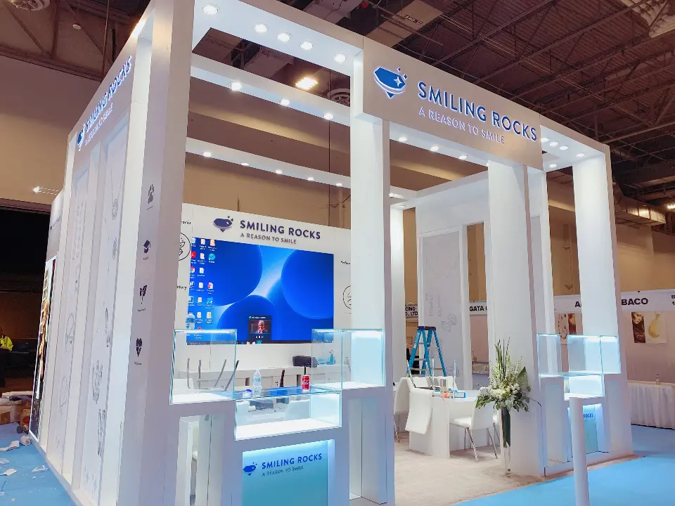 Angled view of the open booth with screen, white seating and lit showcases