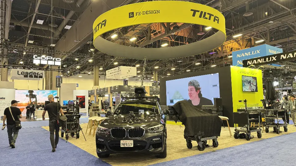 Show-day aisle view of Tilta booth with SUV, camera carts and lit video screen