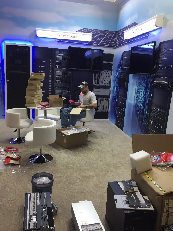 During installation: unpacked boxes and white furniture on the floor of the booth