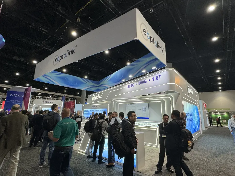 Open side of the booth under the white eoptolink header with visitors at counters