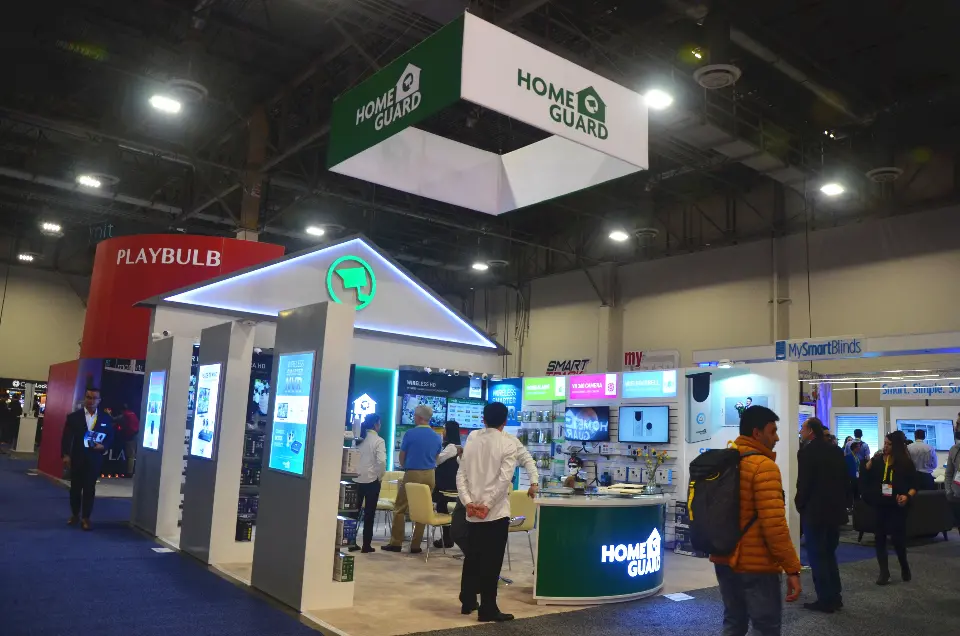 Home Guard booth at CES 2017 with lit house-shaped gable, green hanging sign and display pillars