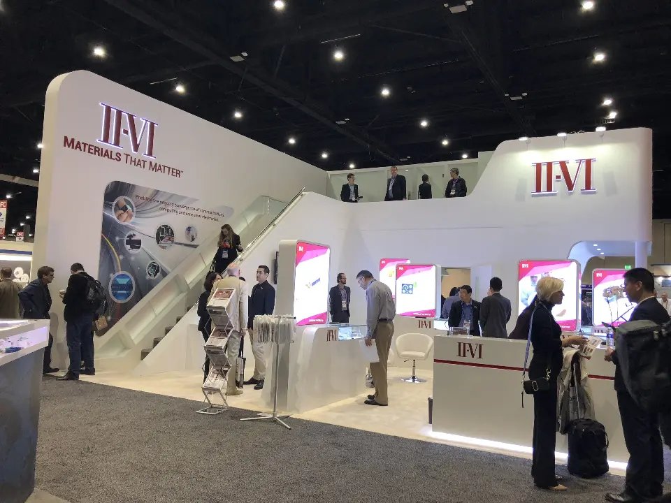 Visitors along the staircase side of the booth beside backlit graphics