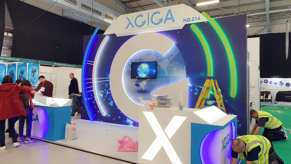 During build-up: XGIGA arch header, glowing arcs and globe backdrop with installers at the counters