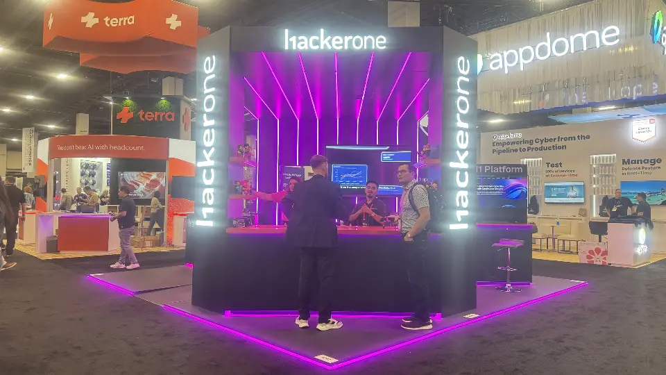 HackerOne booth front with lit hackerone lettering and magenta light lines around the counter