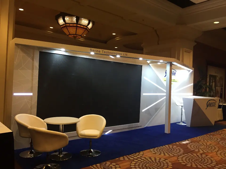 Sarine booth corner with dark screen panel, white lounge chairs and blue carpet