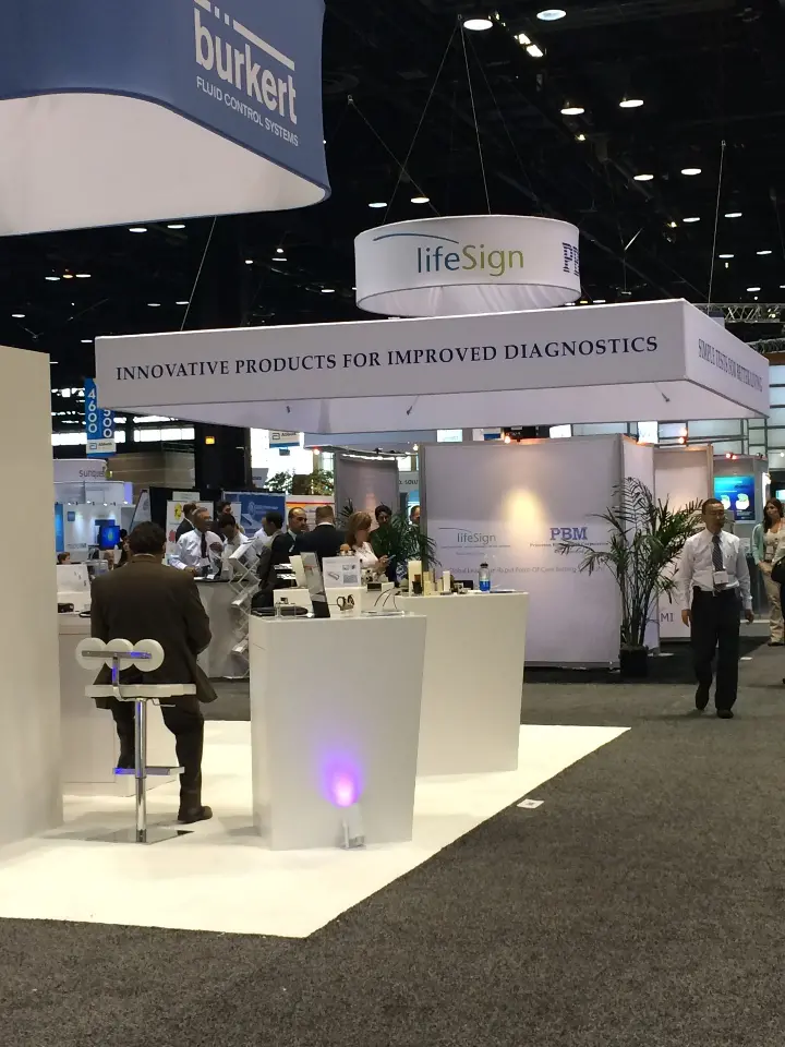 Portrait view of the white booth with plinths, glowing pedestal and hanging sign above