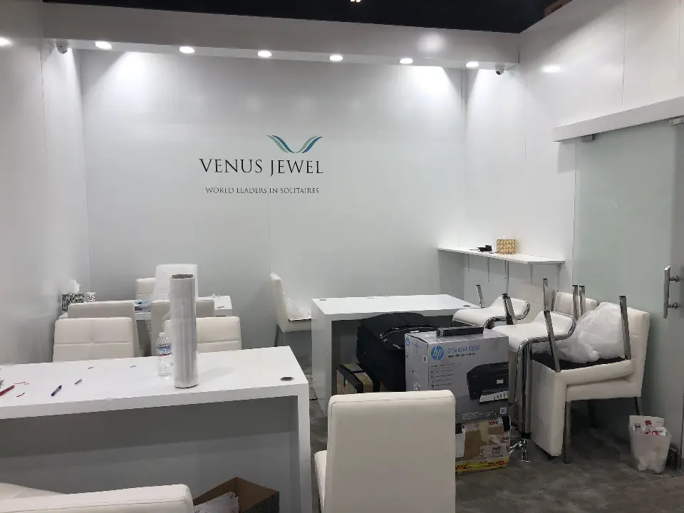 White meeting room with Venus Jewel logo wall, tables and white chairs