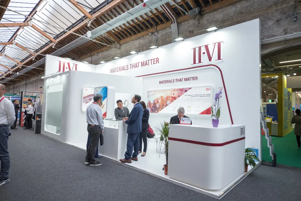 Visitors talking in front of the burgundy-striped counter under the II-VI logo
