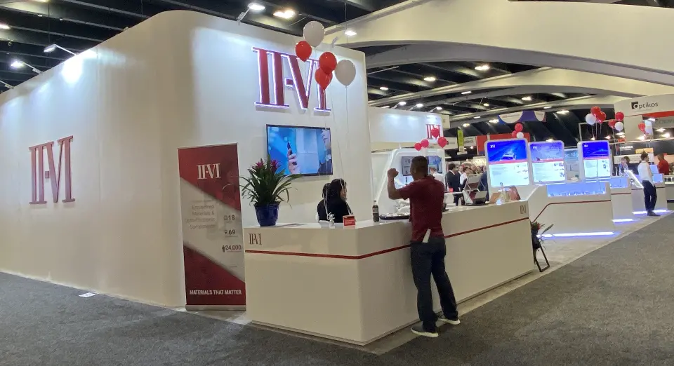 Front counter with plant, wall screen and balloons beside a II-VI banner