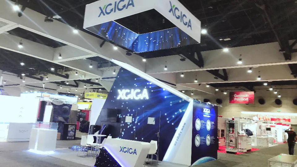 Angled dark blue graphic wall with a square XGIGA hanging sign and a white counter