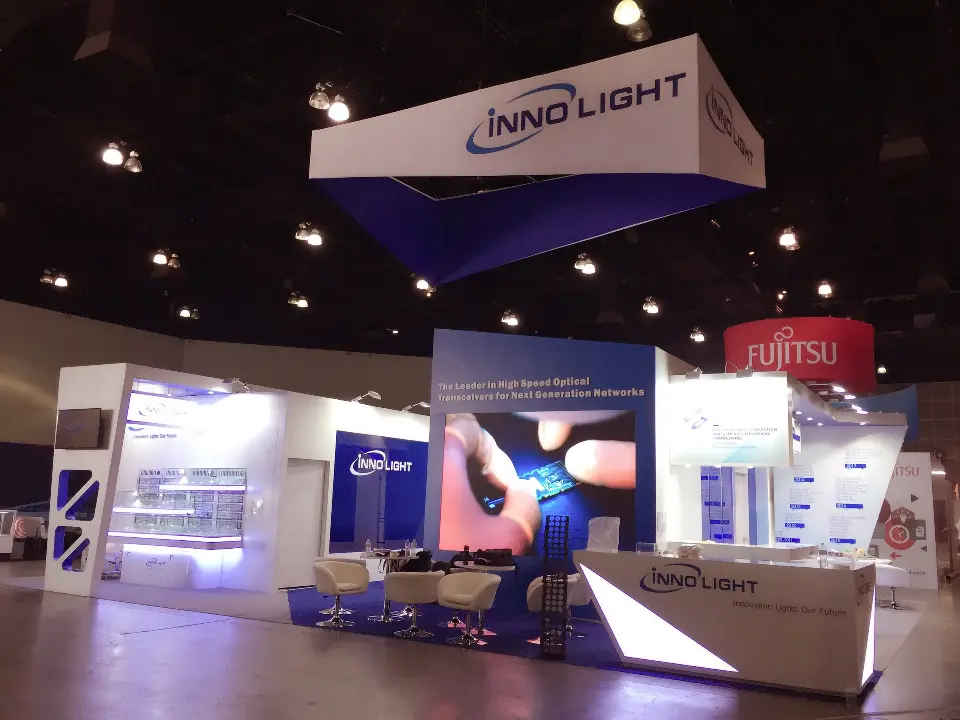 InnoLight booth with white lounge chairs, video screen and lit reception counter