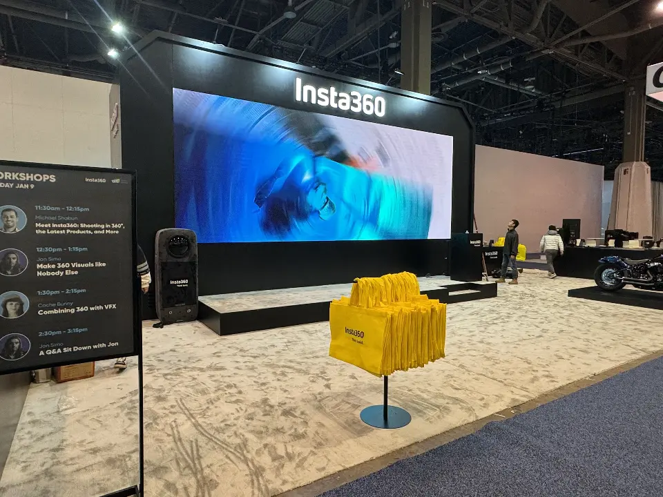 Video screen beside an info panel and a stand of yellow tote bags