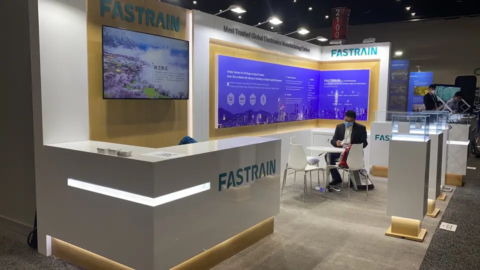 Angled view of the Fastrain stand showing the counter, wall screen, meeting tables and glass pedestals
