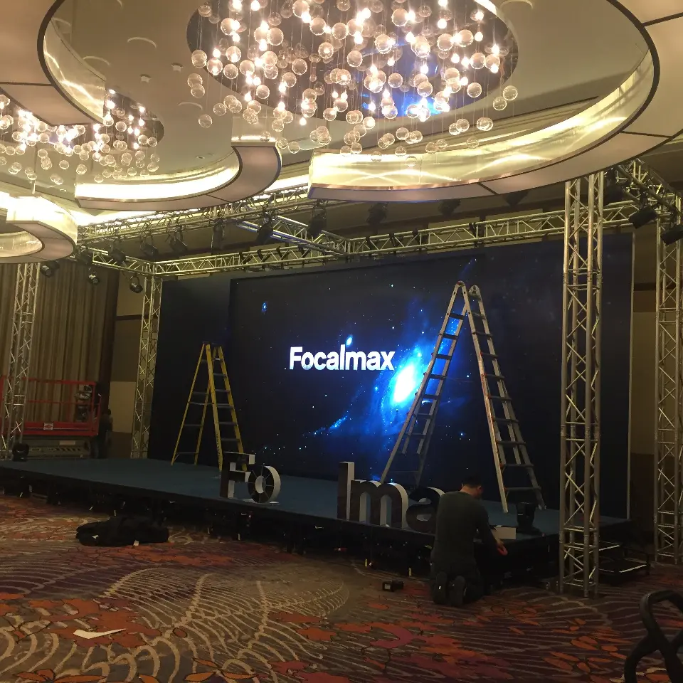 Wide view of the truss-framed stage and screen beneath the ballroom chandeliers