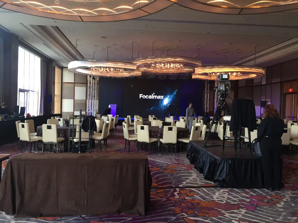 Ballroom with banquet tables and the lit Focalmax screen across the room