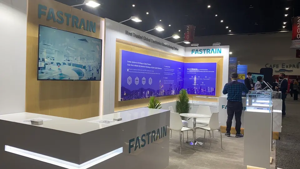 Wide view of the FASTRAIN booth with counter, screen, showcases and tables