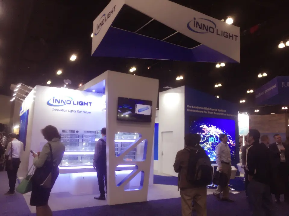 Busy aisle view with a large screen and white booth walls