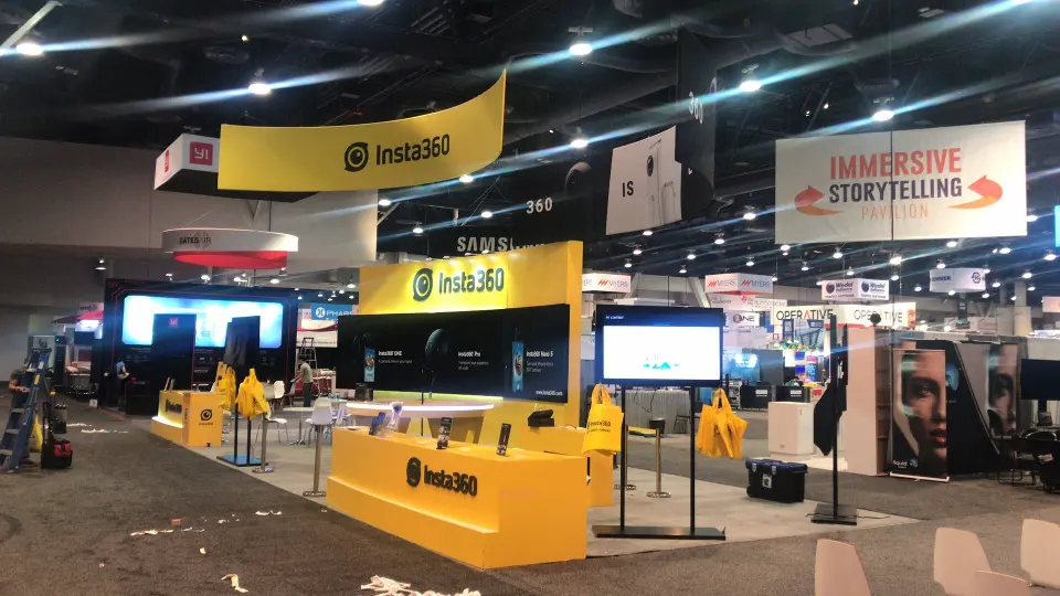 Insta360 booth with yellow hanging banners, long yellow counters and black graphic walls