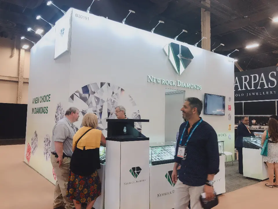 Visitors at the glass showcases below the green diamond logo on the booth corner
