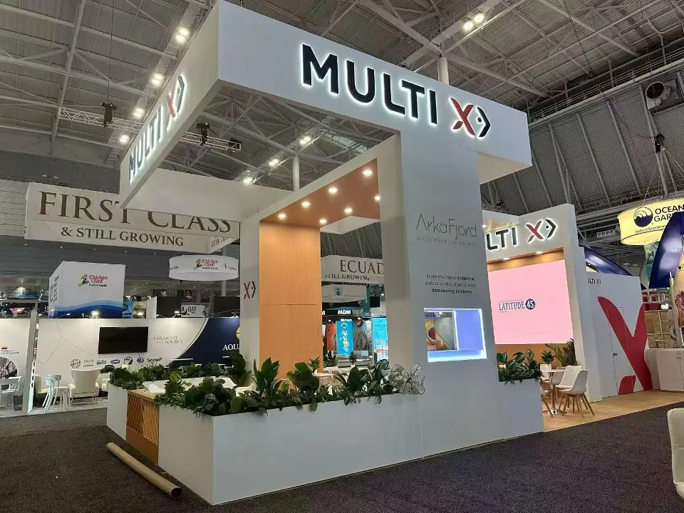 Corner of the white Multi X booth with planters, wood-look wall and a pink video screen