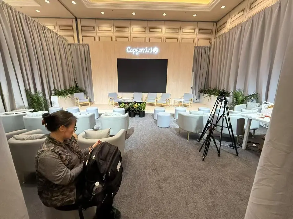 Lounge with white sofas and a large screen while a guest works on a laptop