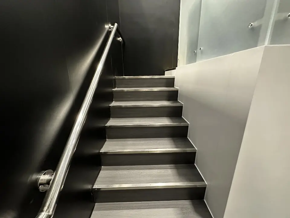 Looking up the black stairs and steel handrail from below