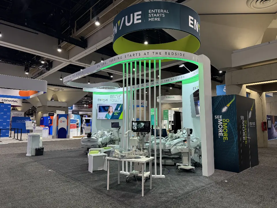Wide view of the ENVUE booth with navy ring sign, curved white band and hospital beds