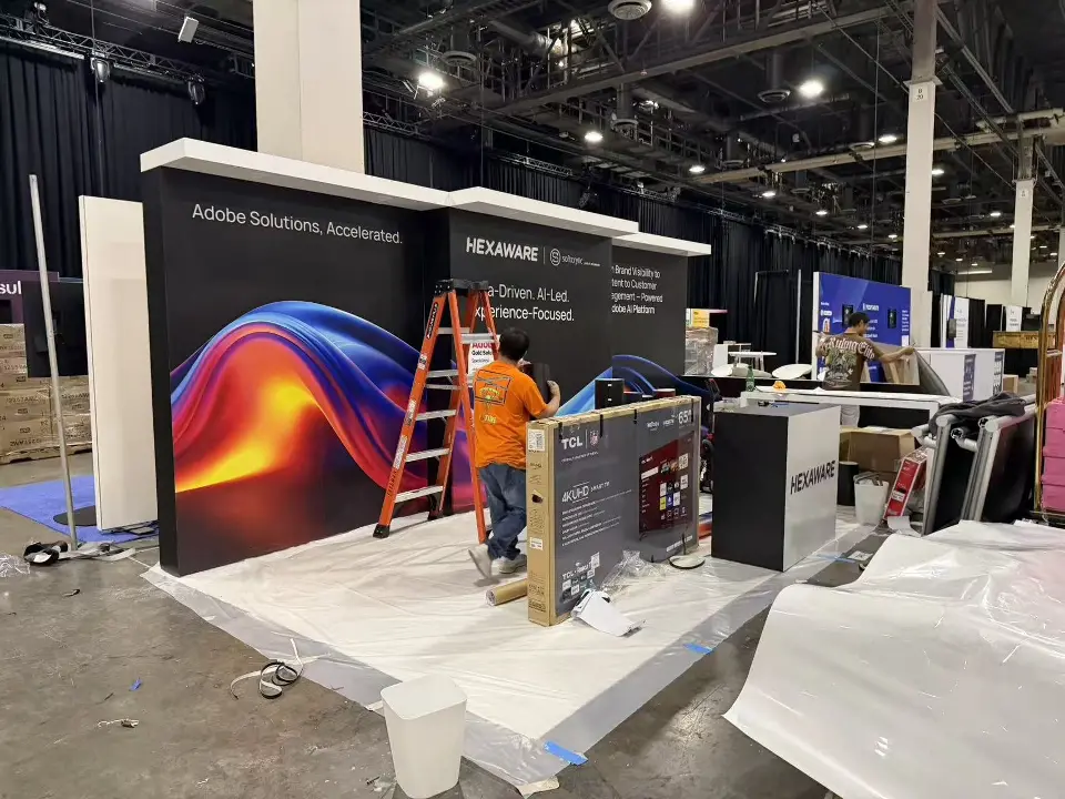 Hexaware booth during final setup with a worker on a ladder beside a swirl graphic wall