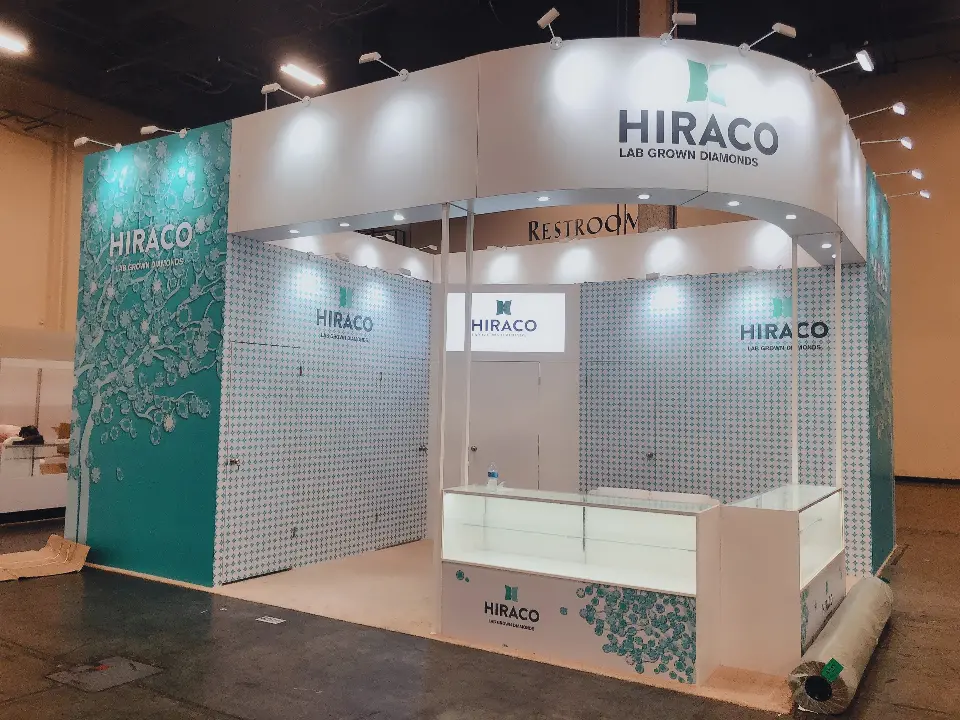 Front corner view of the HIRACO booth with white curved header and teal patterned walls