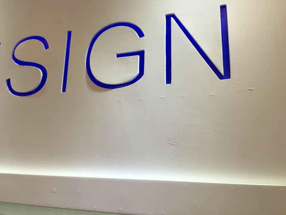 Close-up of blue DESIGN lettering on the white wall above a light strip