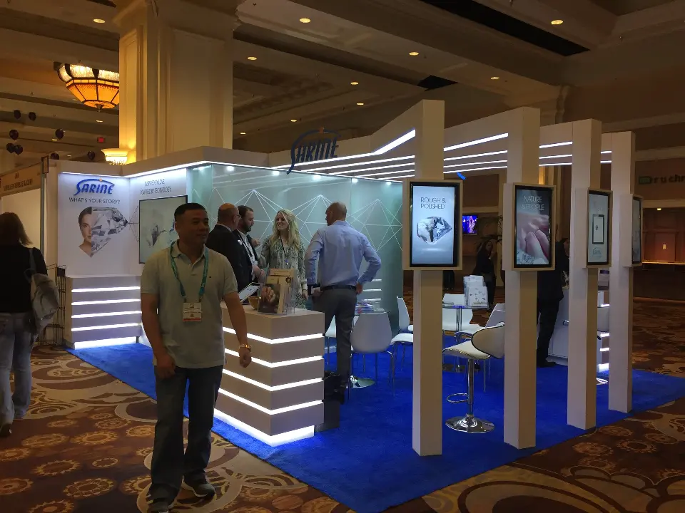 Staff member in the aisle beside lit Sarine counters and tall display screens
