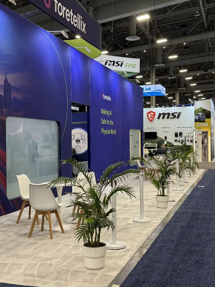 Booth corner with a potted palm and white chairs on light flooring