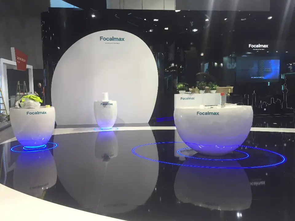 White Focalmax pods and round planters standing in blue light rings on the glossy black floor