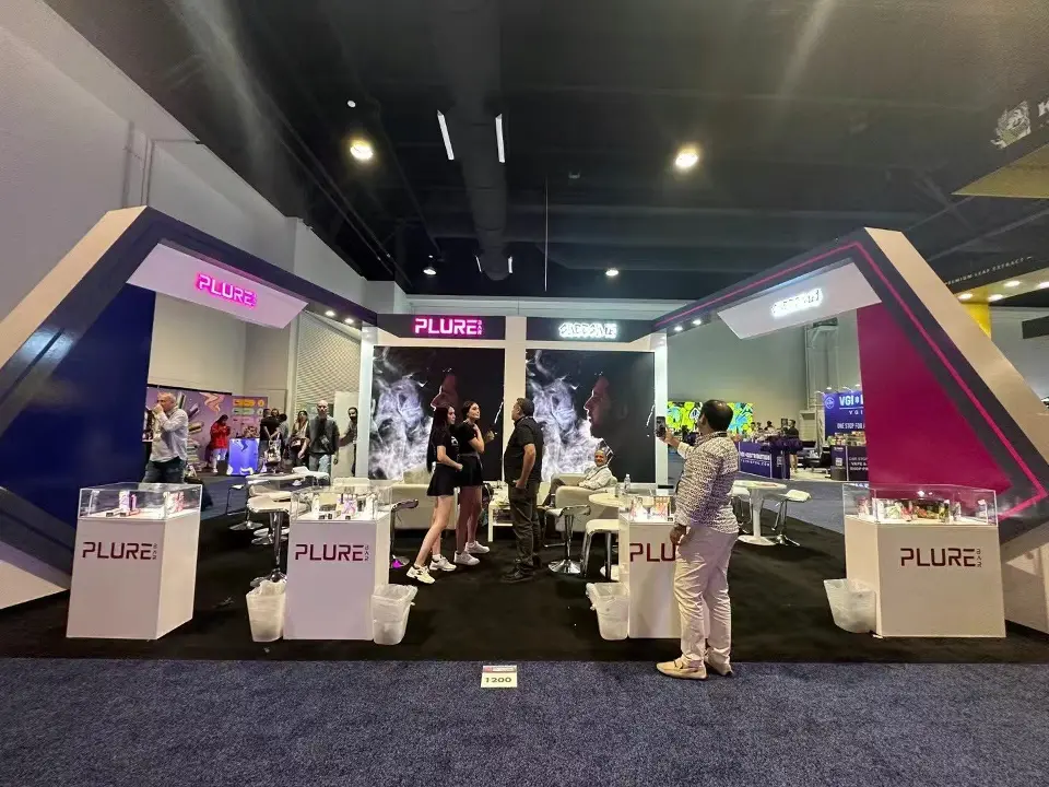 PLURE booth front with white logo plinths, back graphics and visitors inside