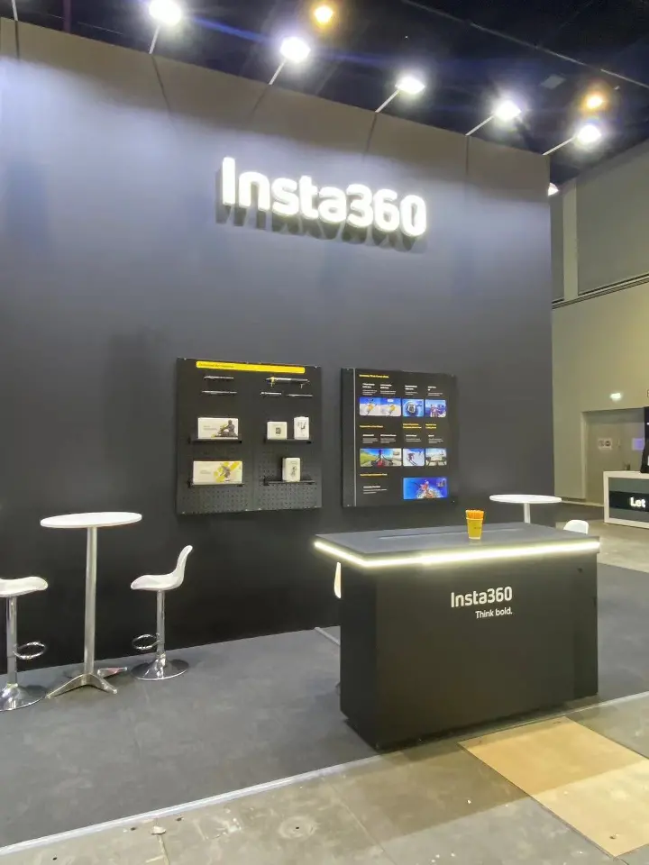 Black wall with product shelves, Insta360 lettering and a white high table with stools