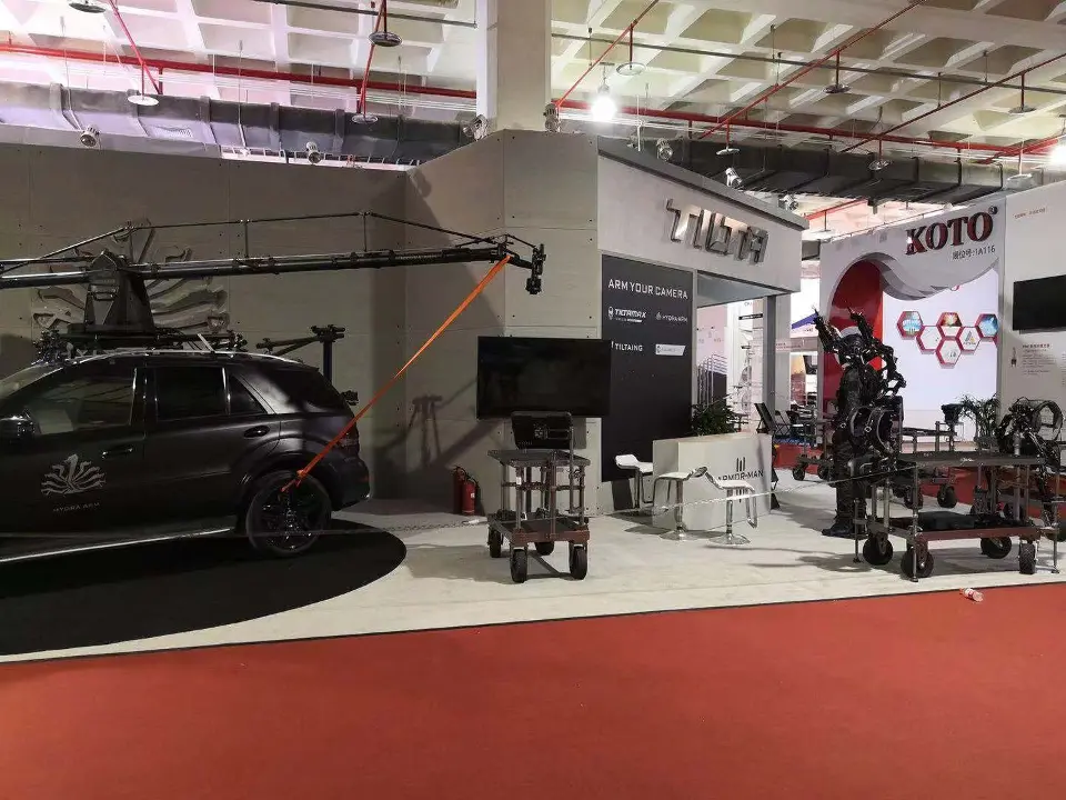 Dark car with camera crane arm on a round platform beside grey walls