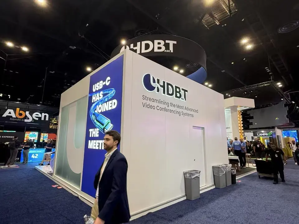 Closed white side of the HDBaseT Alliance booth with a blue USB-C graphic panel and HDBT logo wall