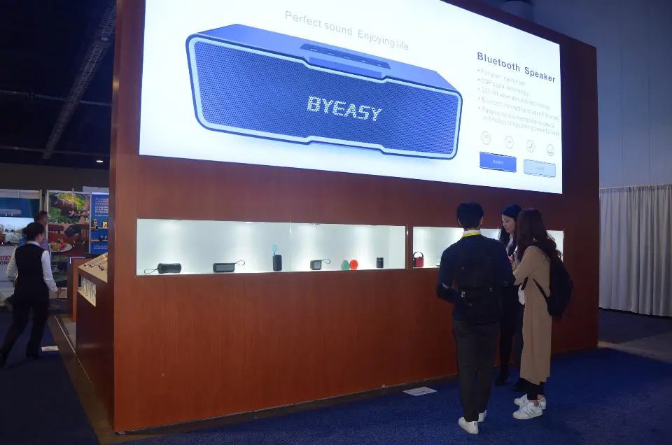 Large backlit speaker graphic over a long product shelf with visitors