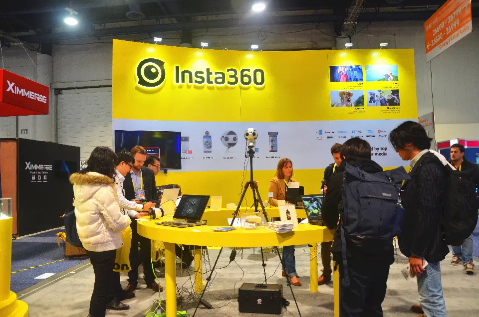 Visitors at the round yellow demo table with laptops and a 360 camera on a tripod