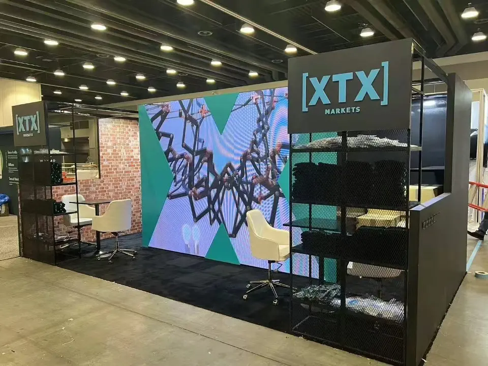 Front view of the XTX Markets booth with teal X graphics around a video wall