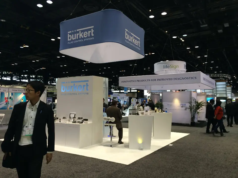 burkert booth with blue square hanging sign, white display plinths and lit back wall