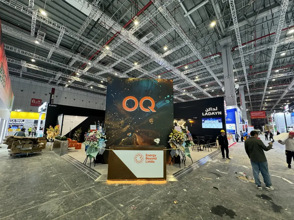 Front corner view of the OQ graphic tower with flower stands and lit welcome counter