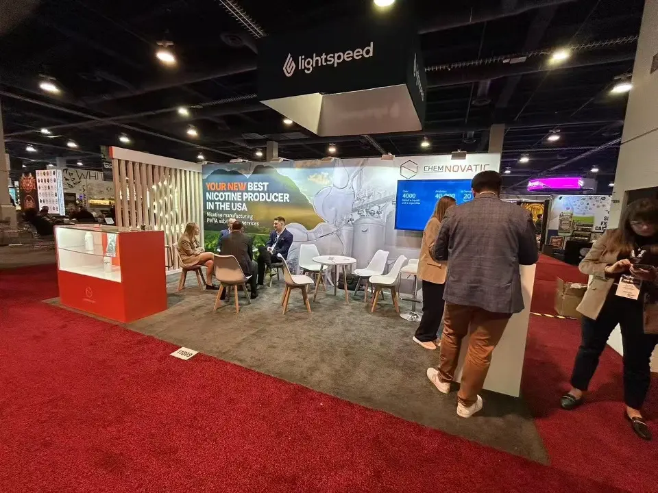 Wider view of the Chemnovatic booth with graphic wall, screen, seating and visitors