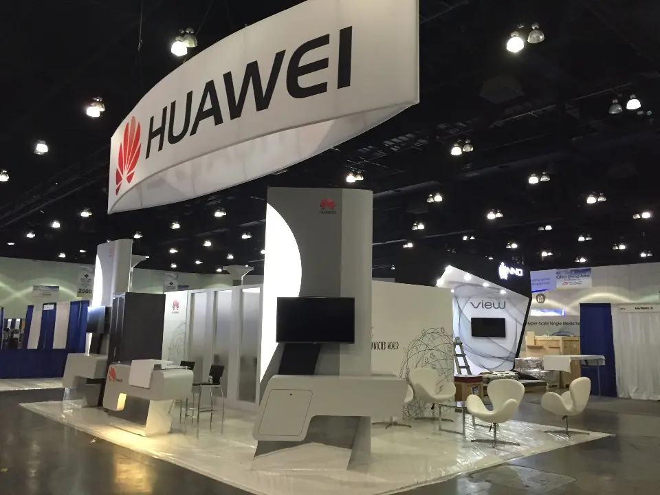 Finished HUAWEI booth with curved white panels, video screens and white lounge chairs