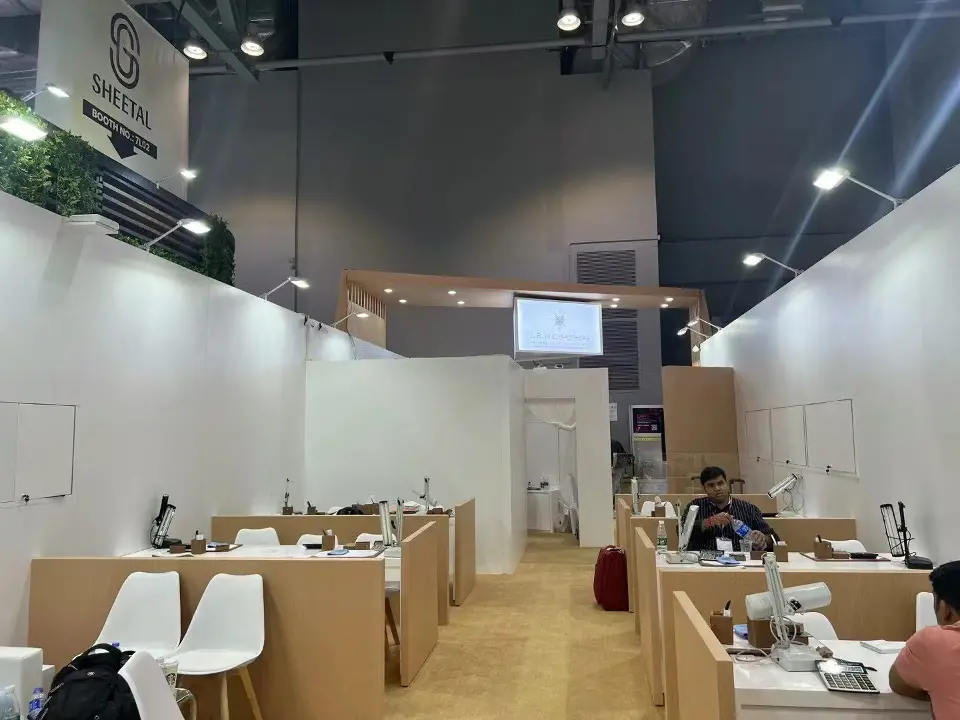 Inside the J.B. and Brothers booth with wood-look desks, white chairs and a screen