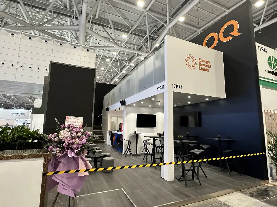 During build-up: OQ booth 17P41 with white overhang, frosted glass railing, bar tables and caution tape