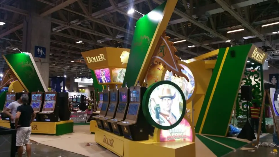Front view of slot machines between green angled panels and a round lit emblem